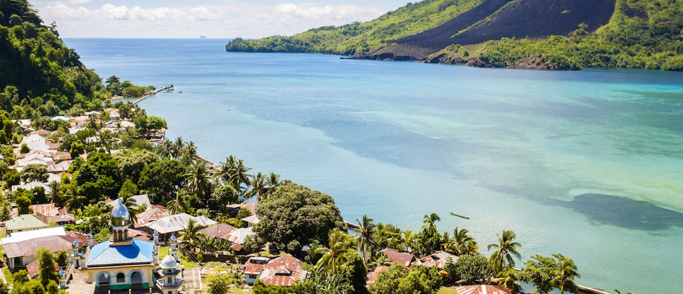 Aerial view of Padang, Indonesia, a coastal town with a mosque, green hills, and clear blue ocean.