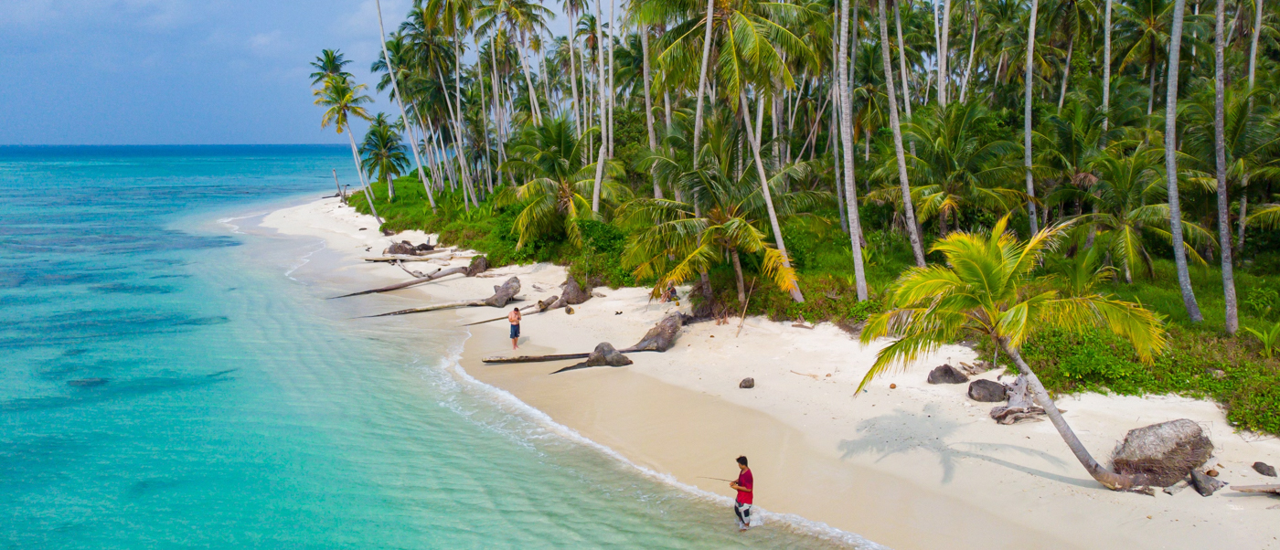 Two people wade in the clear turquoise water on a white sand beach in Sungai Pinang.
