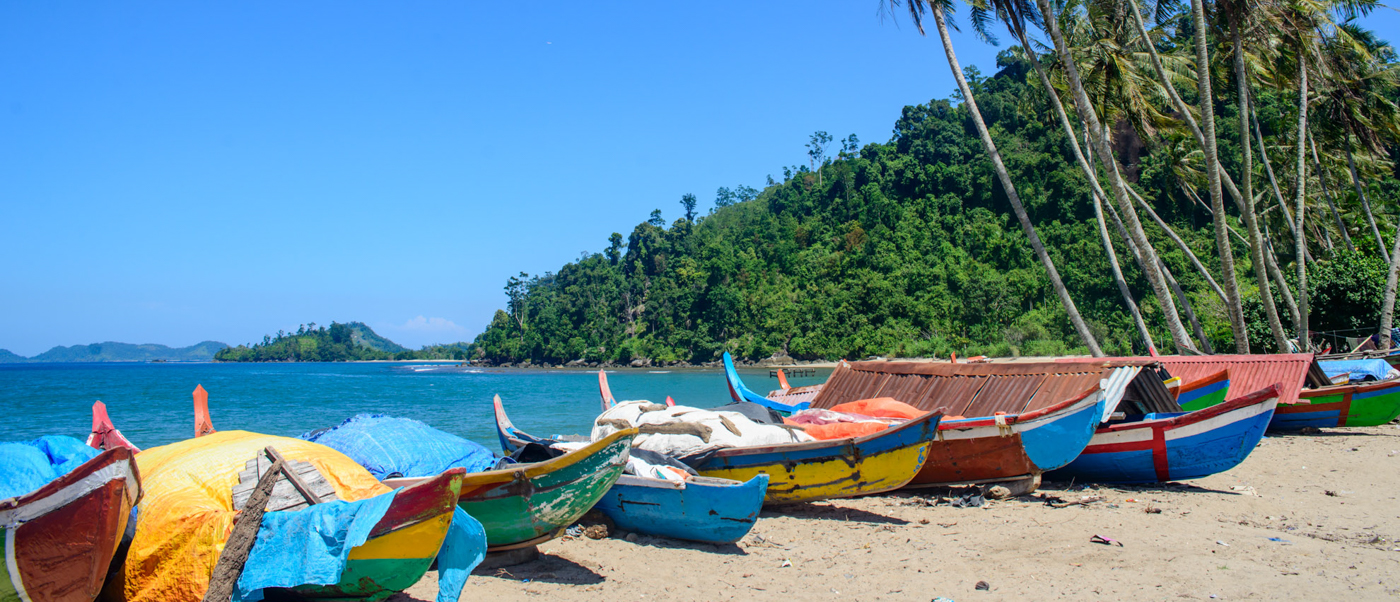 Vibrant fishing boats line the sandy shore of Sungai Pinang, backed by lush hills and clear water.