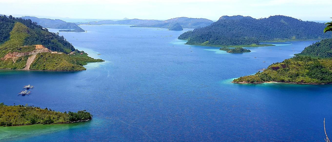 Tropical bay in Sungai Pinang with clear blue water, jungle-covered islands, and two small boats.