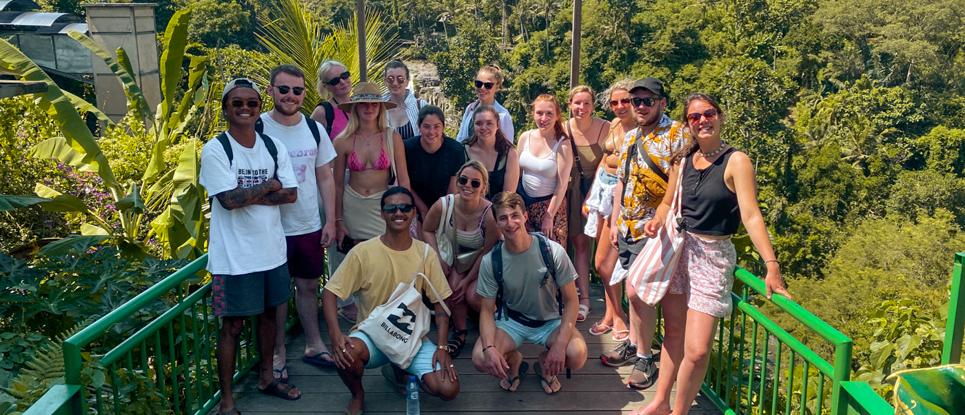 A happy group of backpackers posing on a bridge overlooking the lush Ubud jungle.