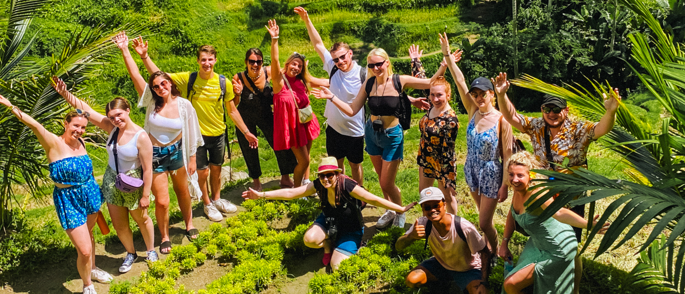 A group of happy young travelers waving and smiling in lush green rice terraces in Ubud, Bali.