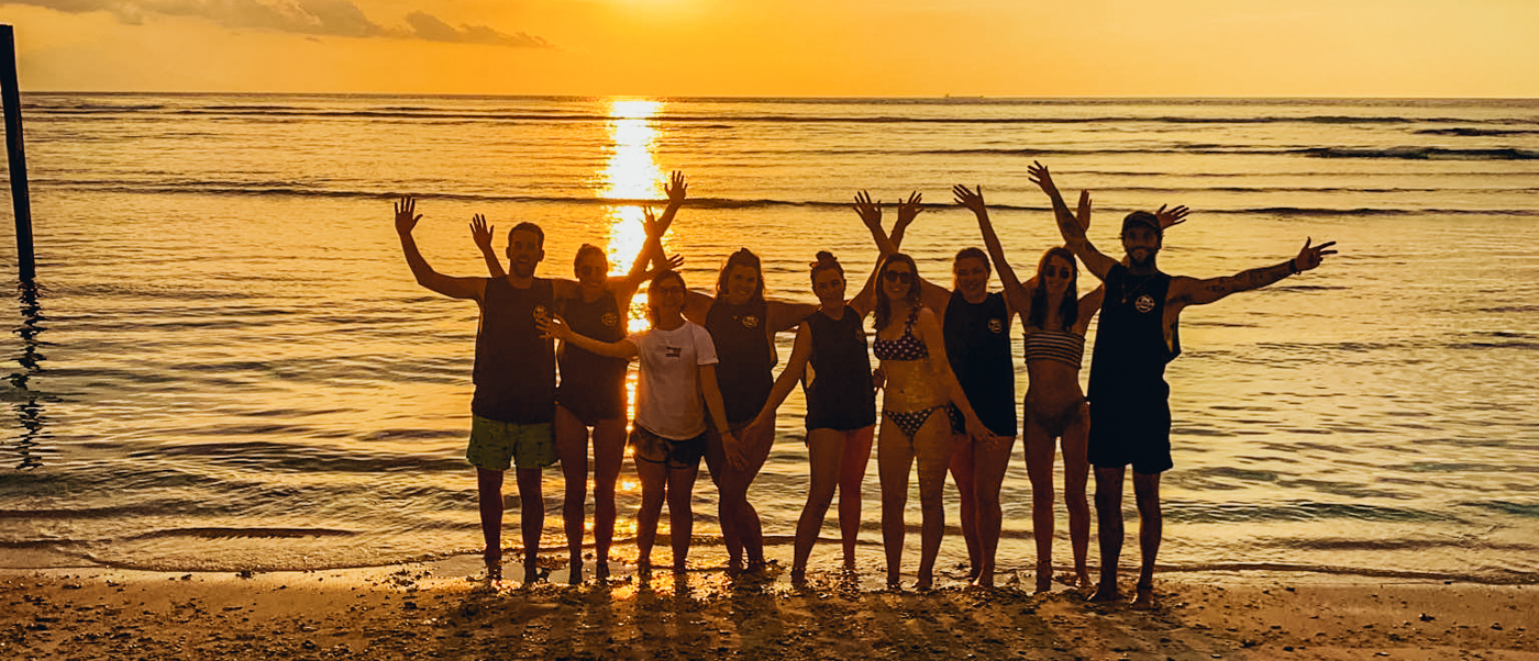 Backpackers celebrate sunset on Gili Trawangan beach, arms raised before the golden ocean.