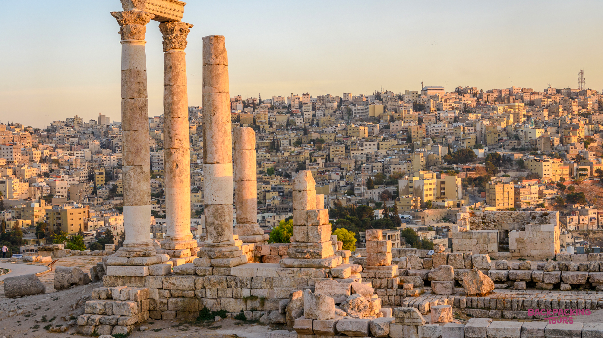 Ancient Roman columns stand tall over the sprawling city of Amman at sunset.