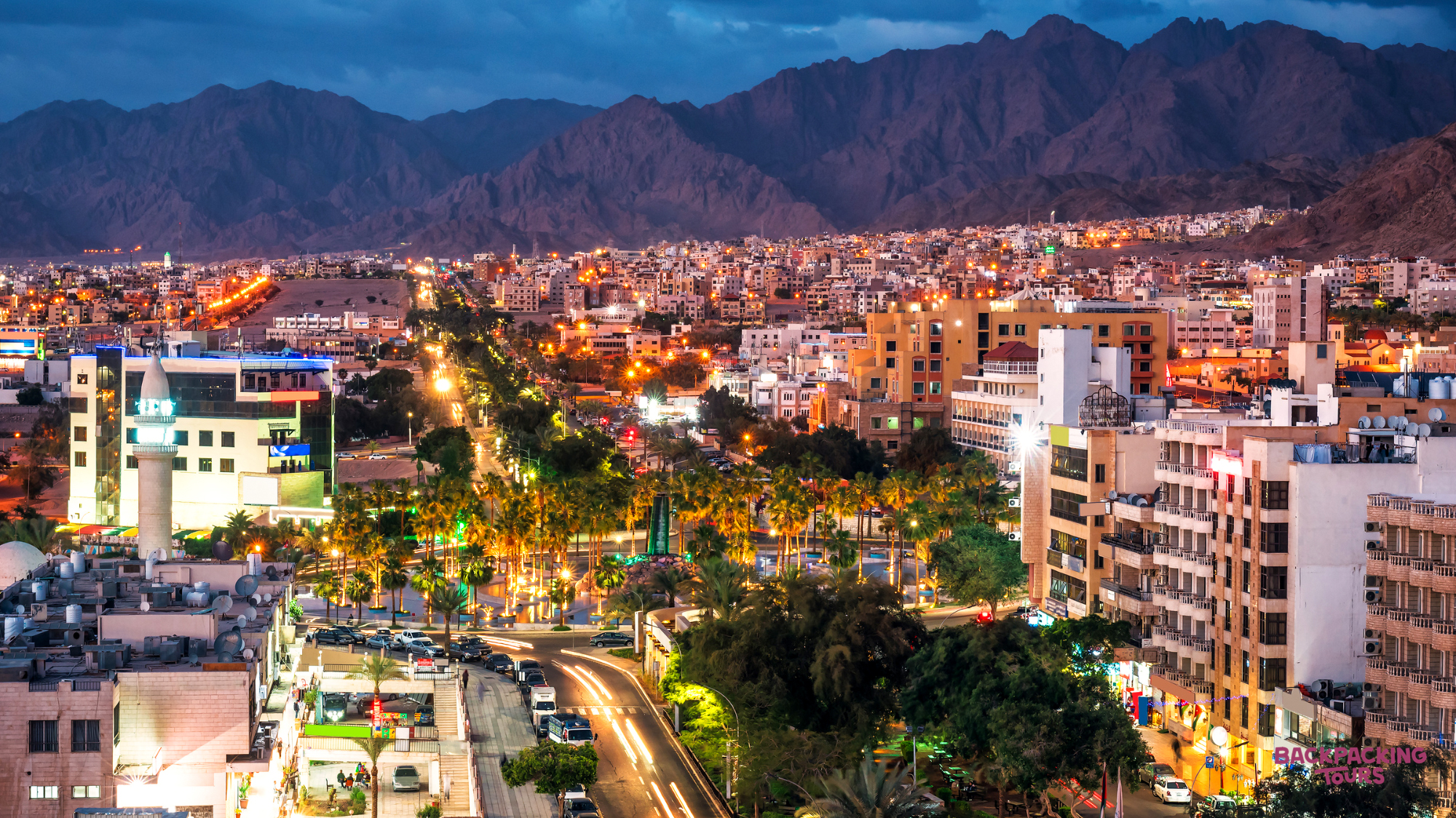 The vibrant city of Aqaba, Jordan, illuminated at night with stunning mountains in the background.