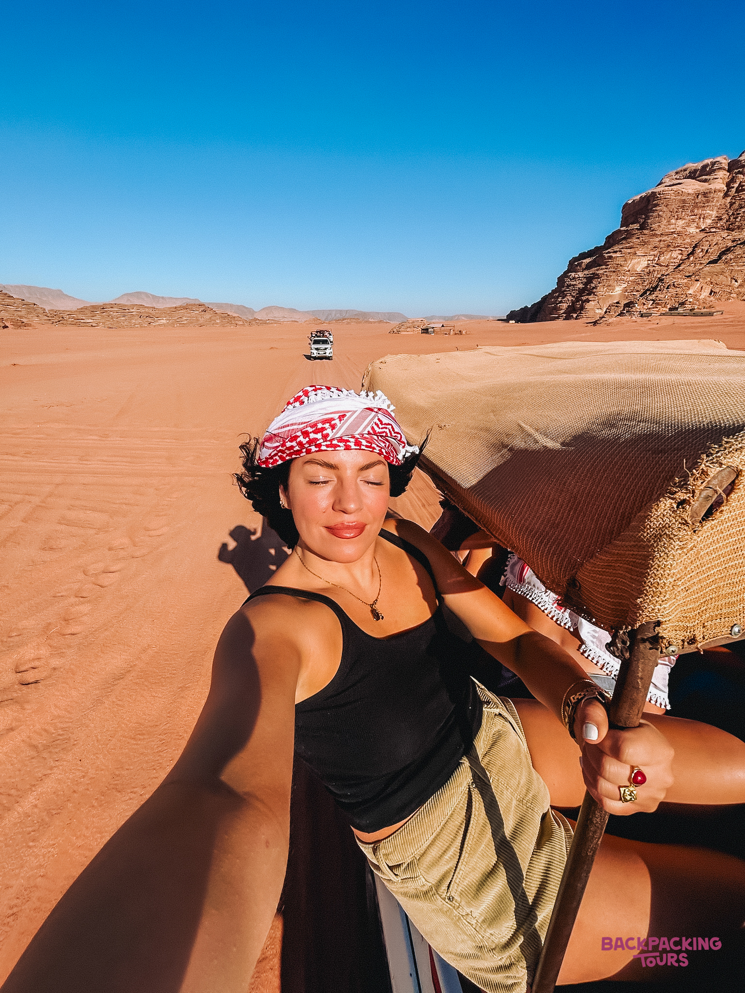 Traveler wearing a keffiyeh enjoying a sunny jeep safari through the red sands of Wadi Rum.