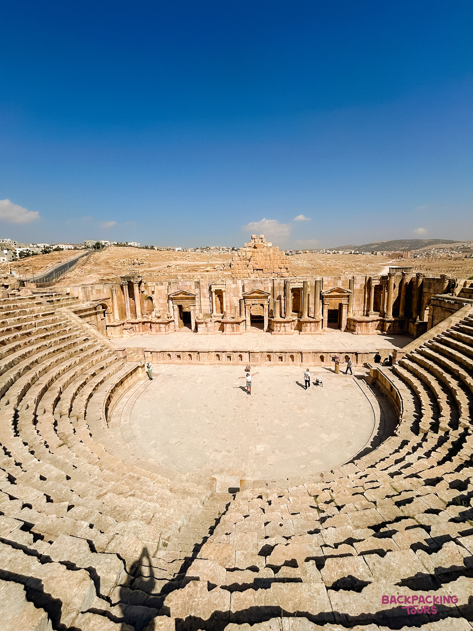 Exploring the grand ancient Roman amphitheatre in Jerash, Jordan, under a bright blue sky.