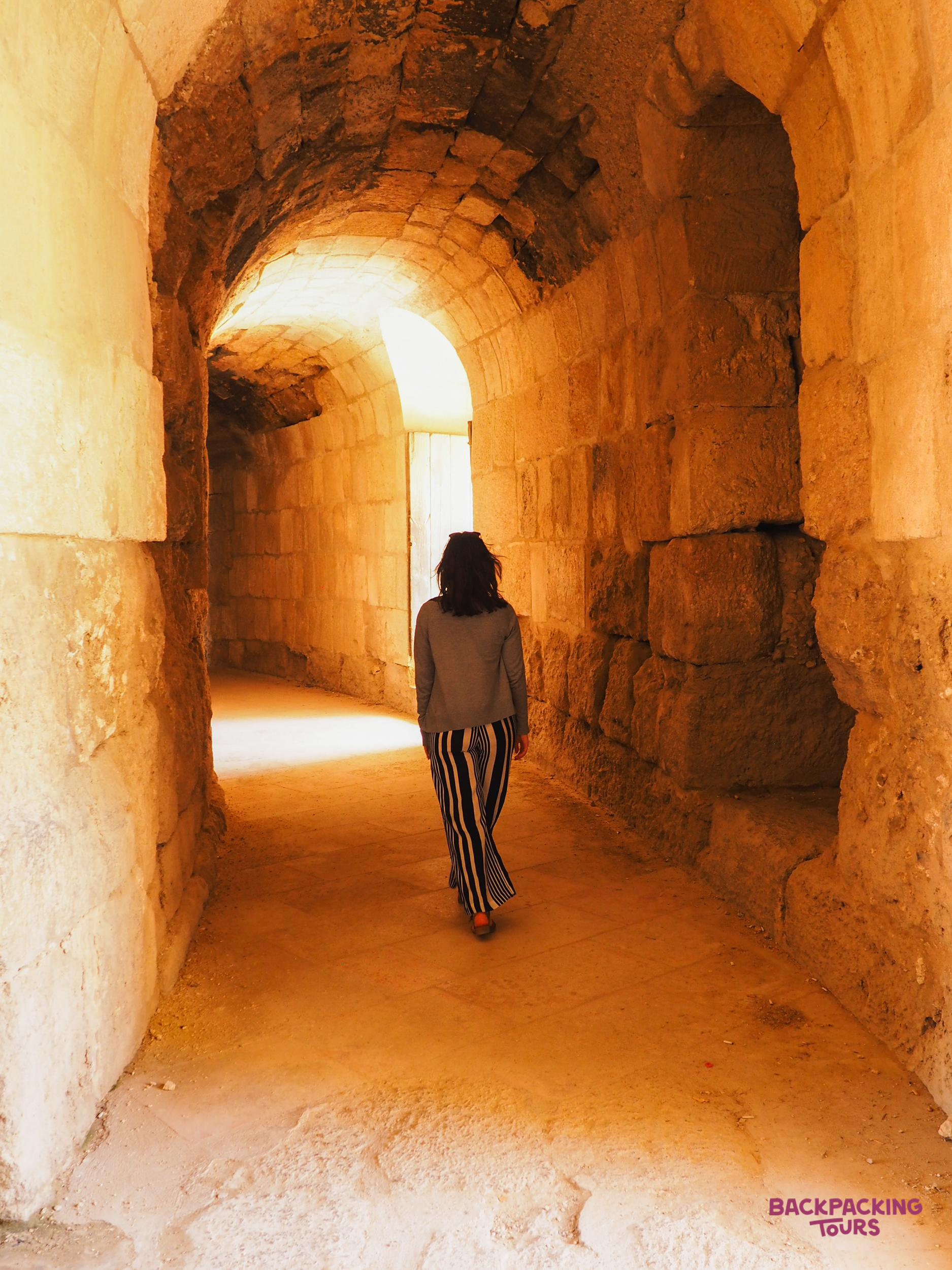 A woman walks through a beautifully lit ancient stone archway at Jerash Roman ruins.
