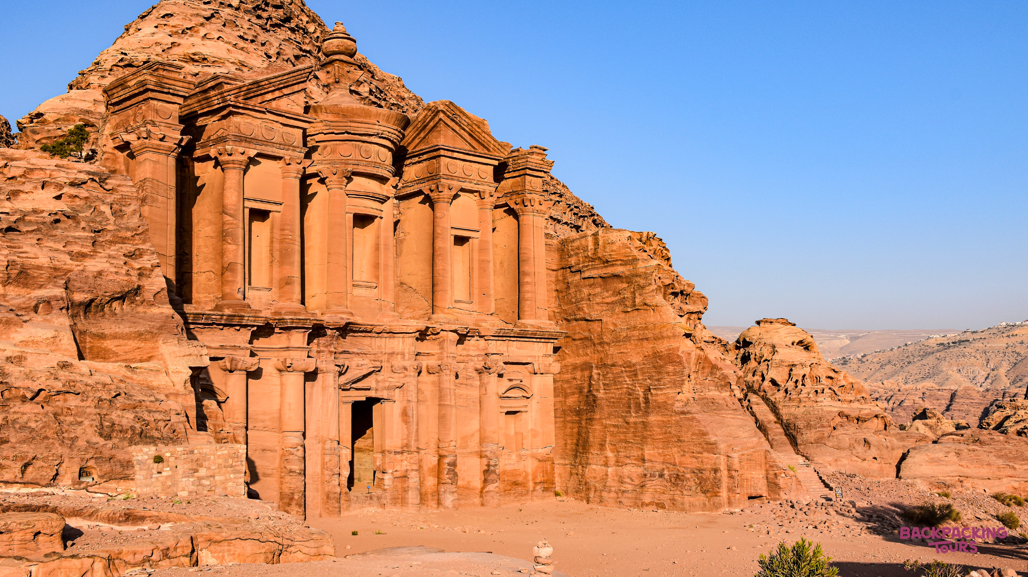 The grand Monastery, carved into the red sandstone cliffs of Petra, Jordan, under a clear sky.