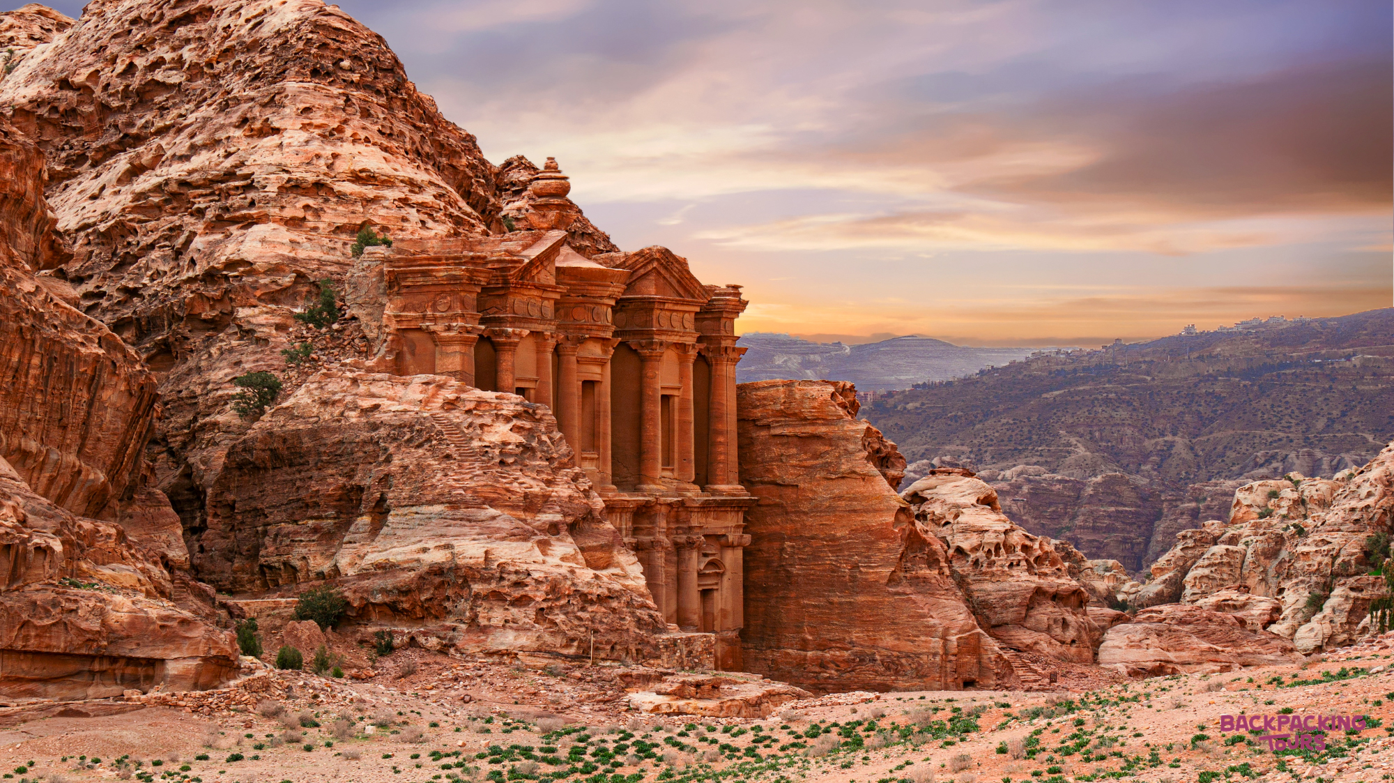 The majestic ancient Monastery carved into the red rock mountains of Petra under a vibrant sunset sky.