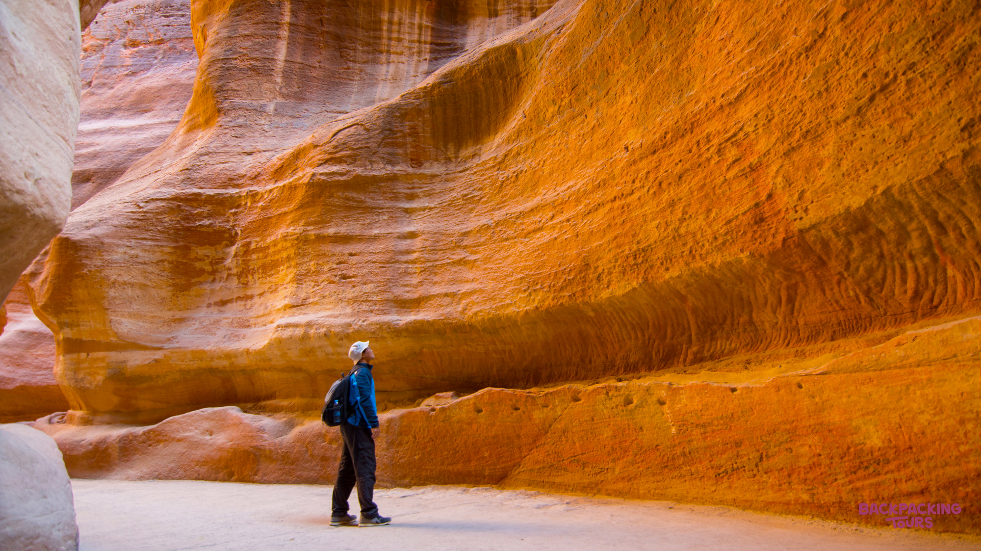A backpacker gazes up at the towering, striated sandstone walls of The Siq in Petra.