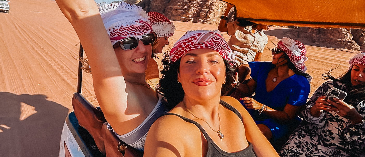 Smiling travelers in traditional headscarves enjoy a desert jeep safari through the red sands of Wadi Rum.