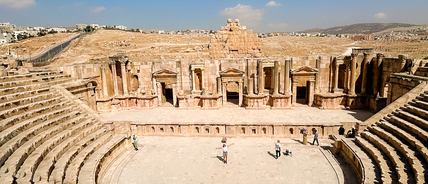 Tourists explore the grand ancient Roman amphitheatre at Jerash, Jordan, under a clear sky.
