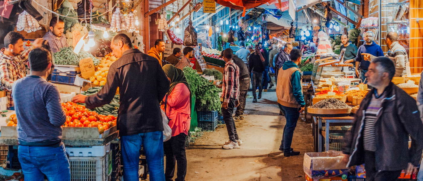 A vibrant market in Amman, Jordan, filled with people browsing stalls of fresh fruits and vegetables.