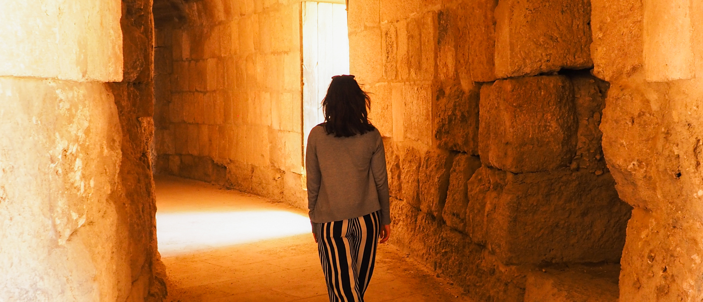 A person walks through a sunlit stone passageway within the ancient Jerash Roman ruins.