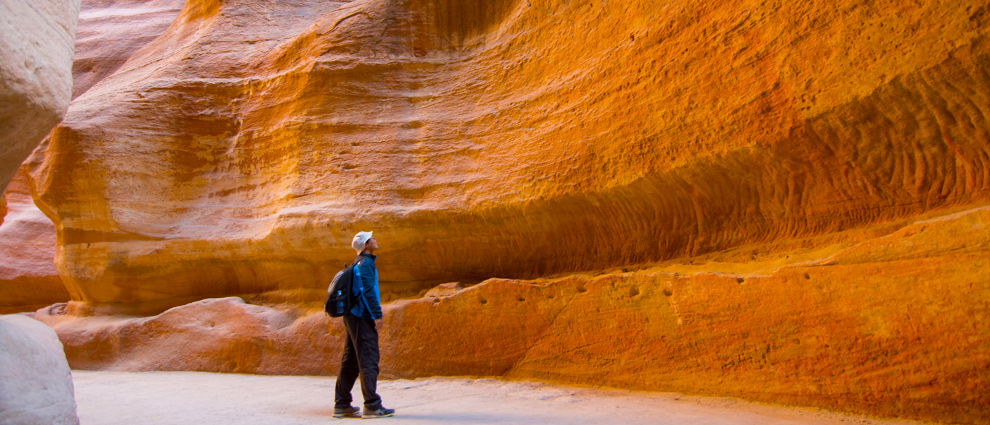 A backpacker looks up at the magnificent, towering red sandstone walls of The Siq in Petra.