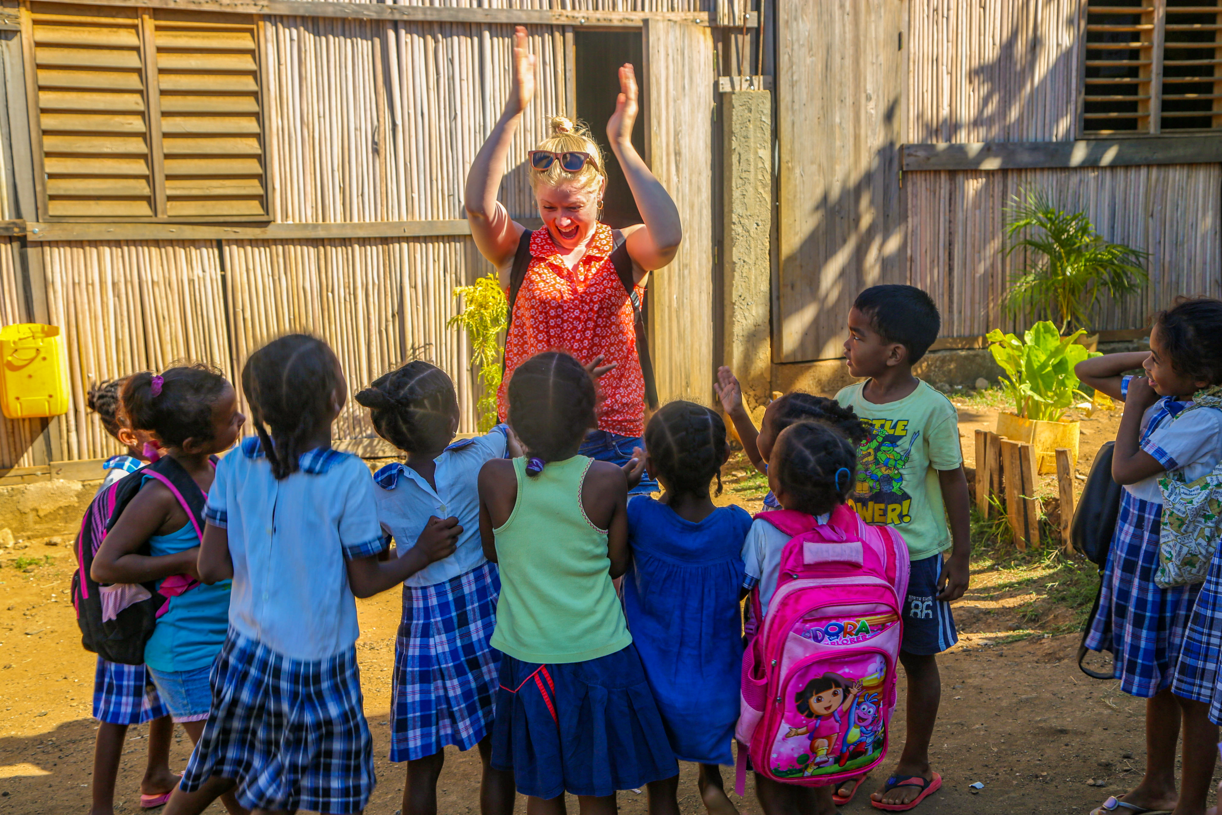 A cheerful volunteer claps hands with smiling children wearing school uniforms in Madagascar.