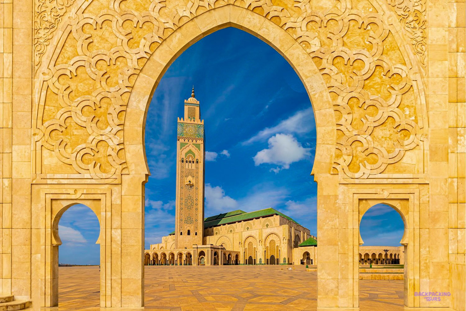 The Hassan II Mosque minaret framed by a carved golden archway under a bright blue sky.