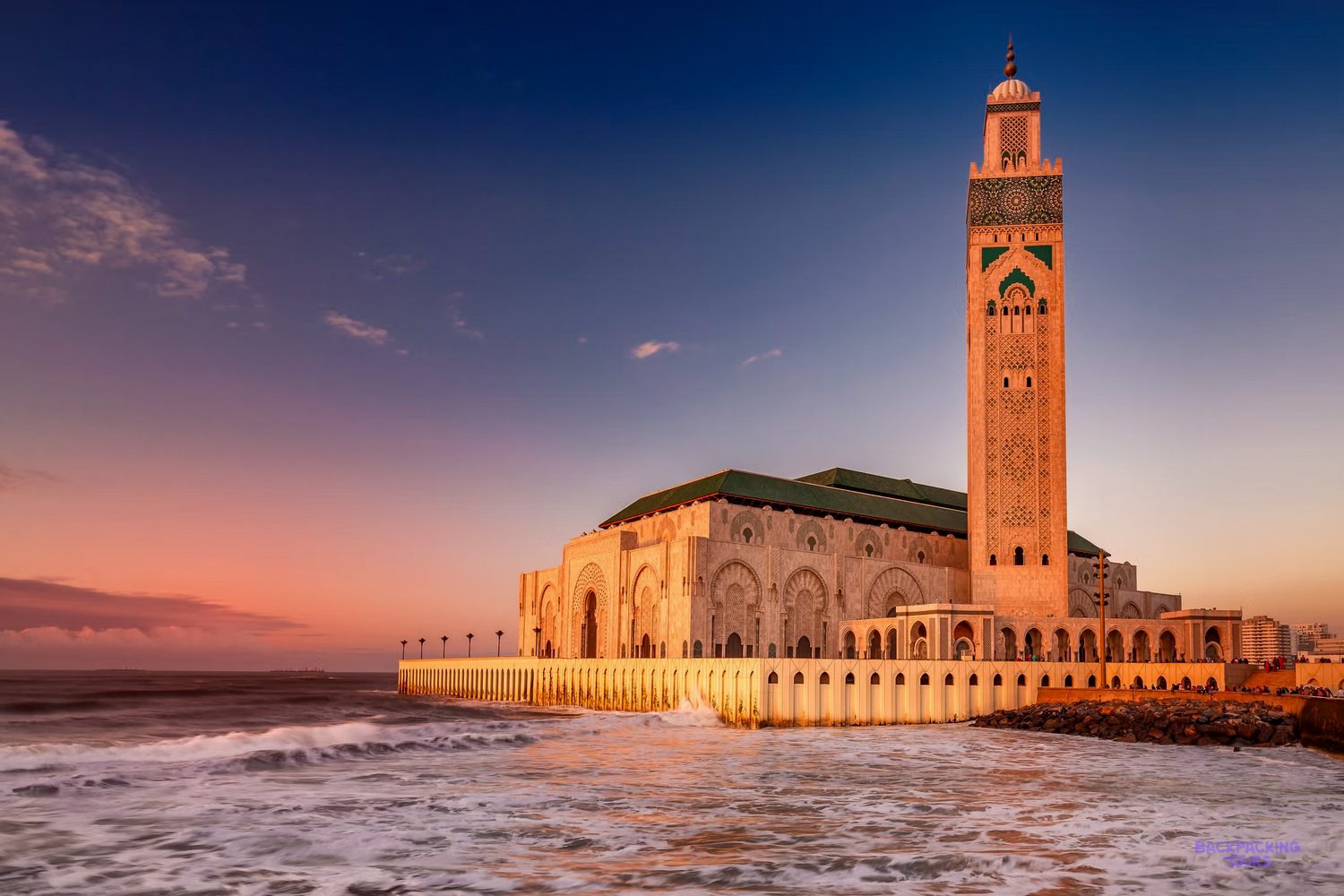 The Hassan II Mosque and its tall minaret beside the Atlantic Ocean in Casablanca at sunset.