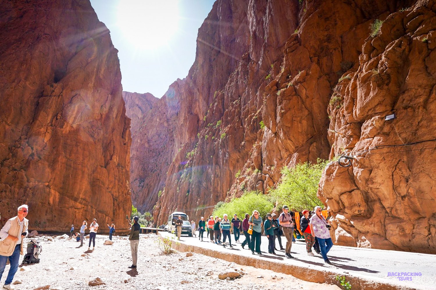 Travellers walk along the floor of Todra Gorge between towering walls of red rock.