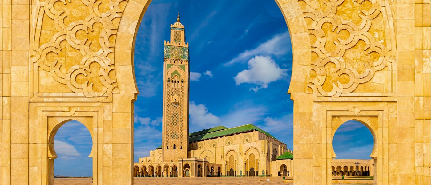 The Hassan II Mosque minaret framed by a carved golden archway under a bright blue sky.
