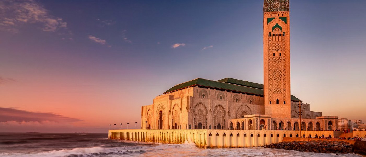 The Hassan II Mosque and its tall minaret beside the Atlantic Ocean in Casablanca at sunset.
