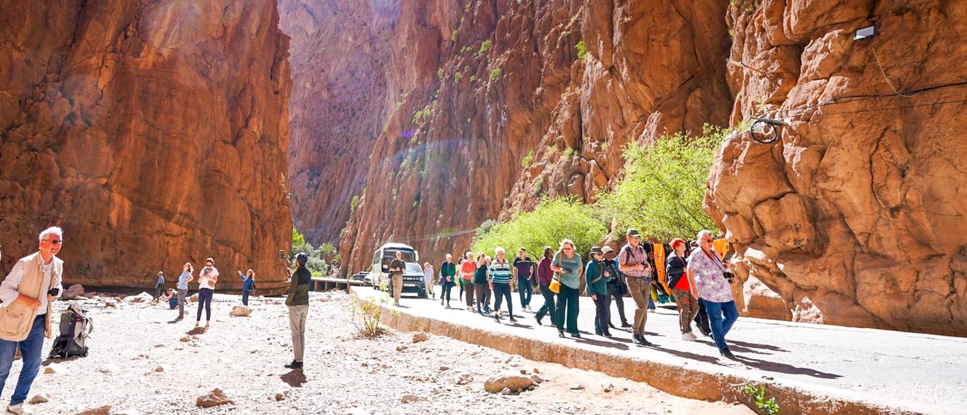 Travellers walk along the floor of Todra Gorge between towering walls of red rock.