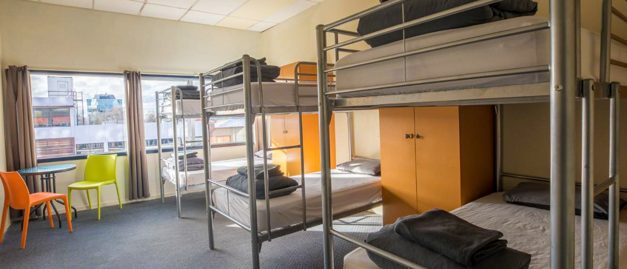 A clean, bright backpacker dorm room in Rotorua with multiple bunk beds and city views.