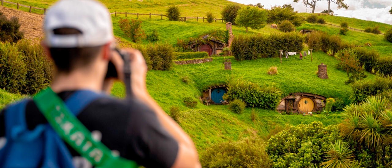 A person photographs the iconic Hobbiton film set with its charming hobbit holes in New Zealand.