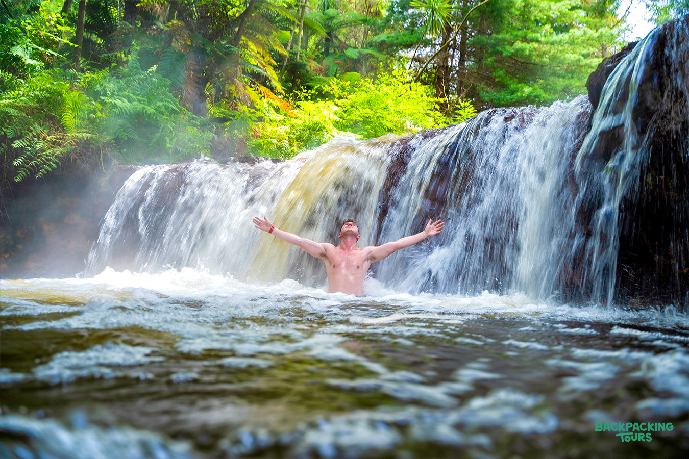 Man enjoying a relaxing soak under a natural waterfall in Rotorua, New Zealand.