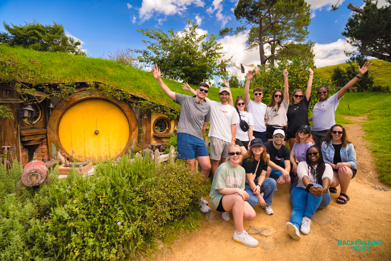 A group of happy backpackers pose in front of a hobbit hole at the Hobbiton film set.