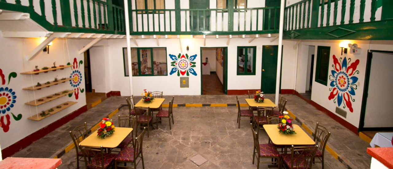 A vibrant hotel courtyard in Cusco featuring colorful murals and tables set for dining.