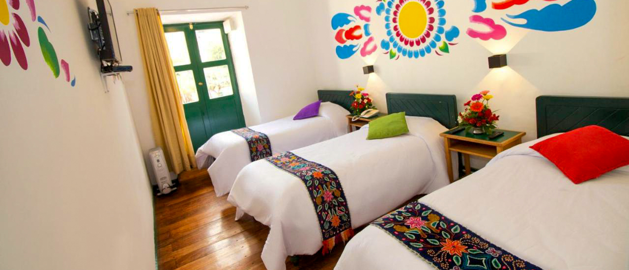 A vibrant hotel room in Cusco, Peru, featuring three beds with colorful runners and wall murals.