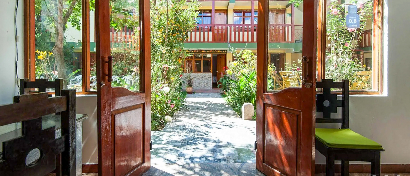 An inviting open wooden door leads to a peaceful hotel courtyard in Ollantaytambo, Peru.