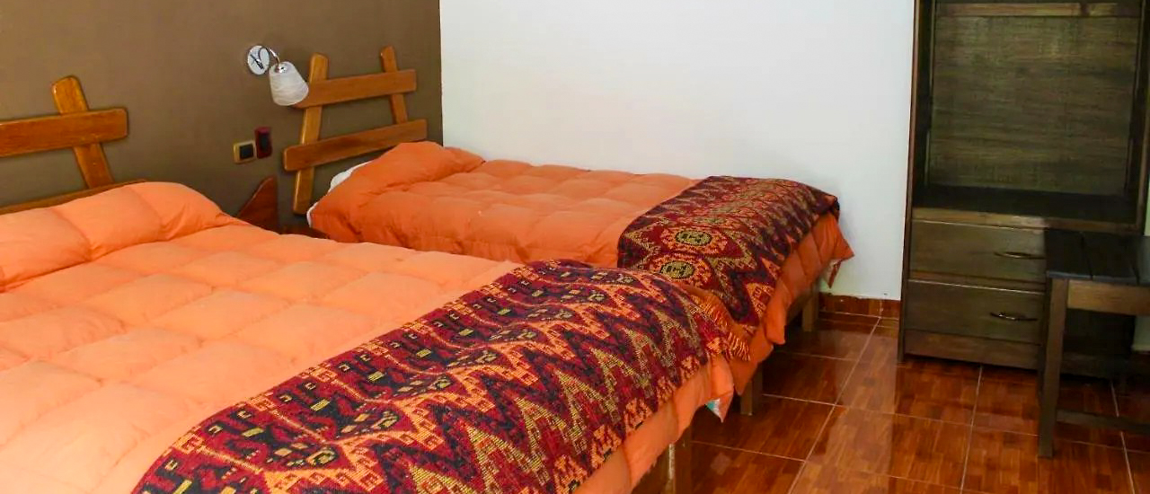 A cozy hotel room in Ollantaytambo with two beds, orange comforters, and patterned throws.