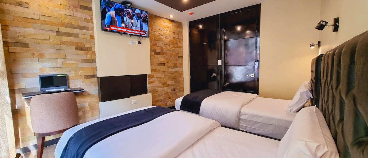 A modern hotel room in Aguas Calientes with two single beds, a TV, and a small desk.