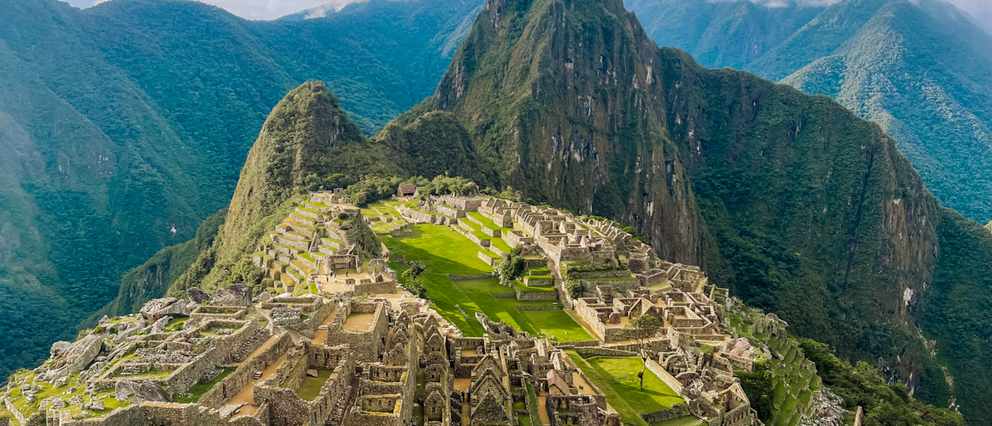 Ancient stone city of Machu Picchu nestled among towering green mountains under a blue sky.