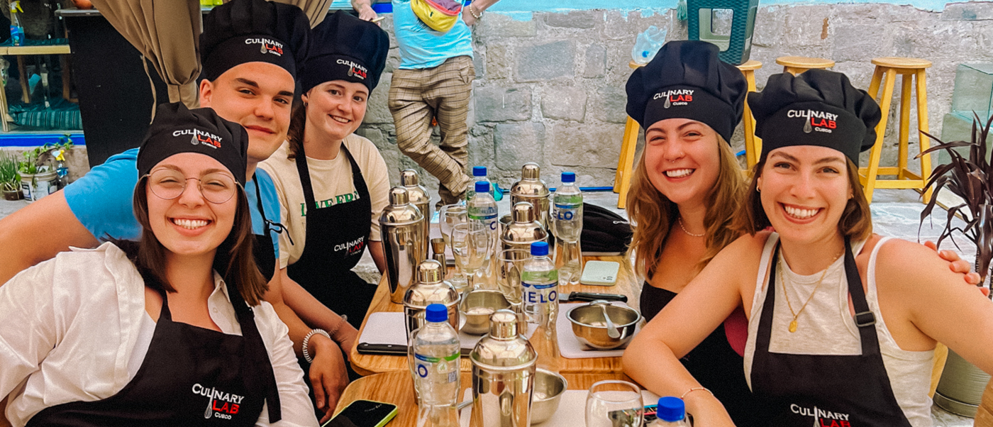 Five happy travelers in chef hats and aprons learning to make pisco sours in Cusco.
