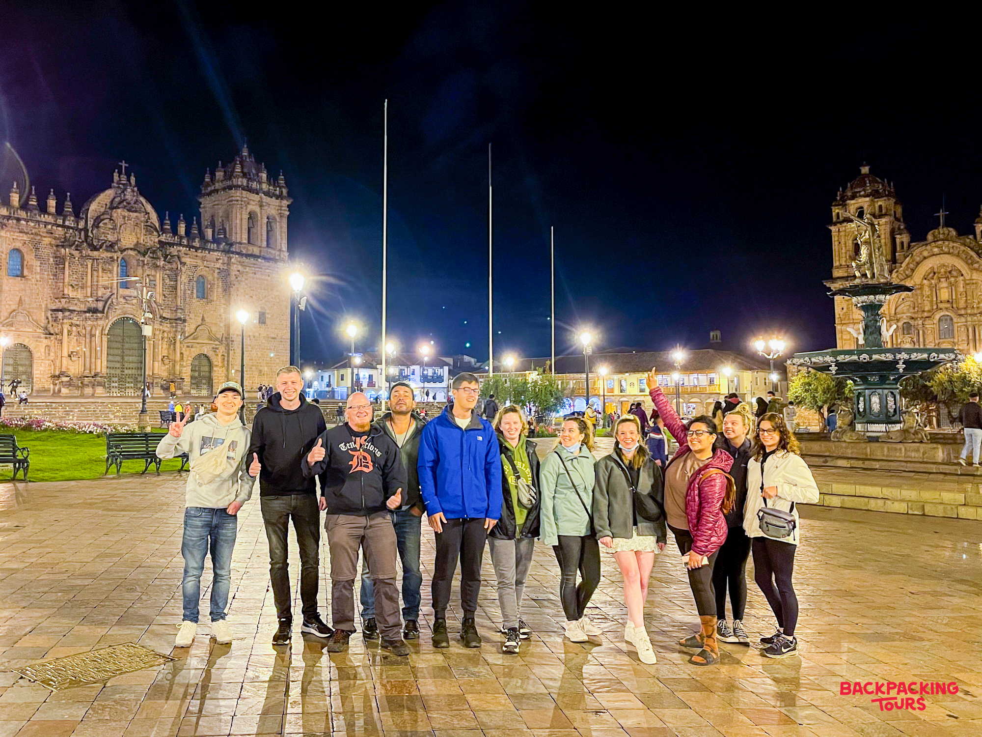Eleven happy travelers pose at night in the brightly lit Plaza de Armas in Cusco.