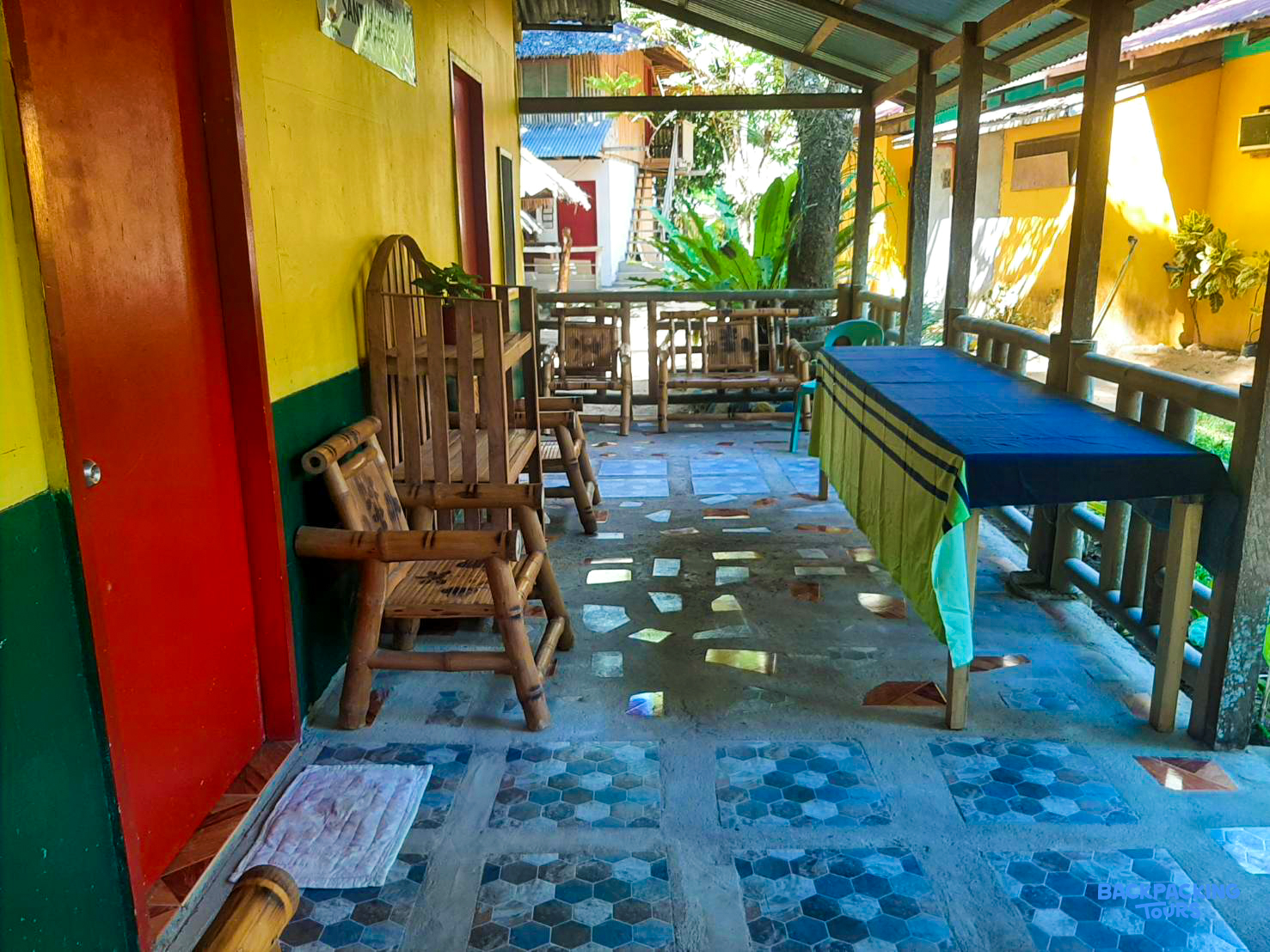 A vibrant outdoor patio with colorful walls, bamboo furniture, and a long table for guests.