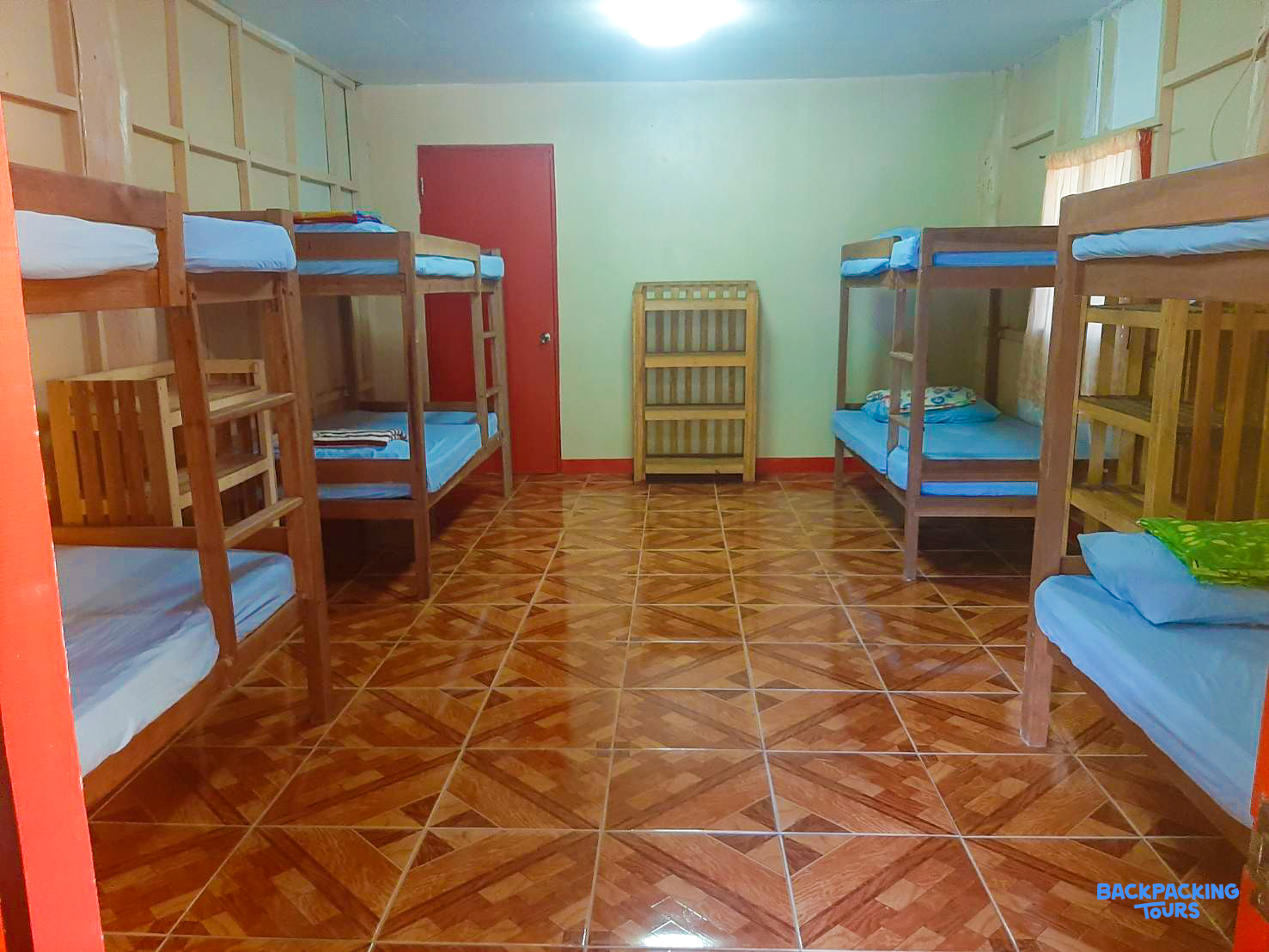 A clean dormitory room with multiple wooden bunk beds and blue mattresses, ready for guests.