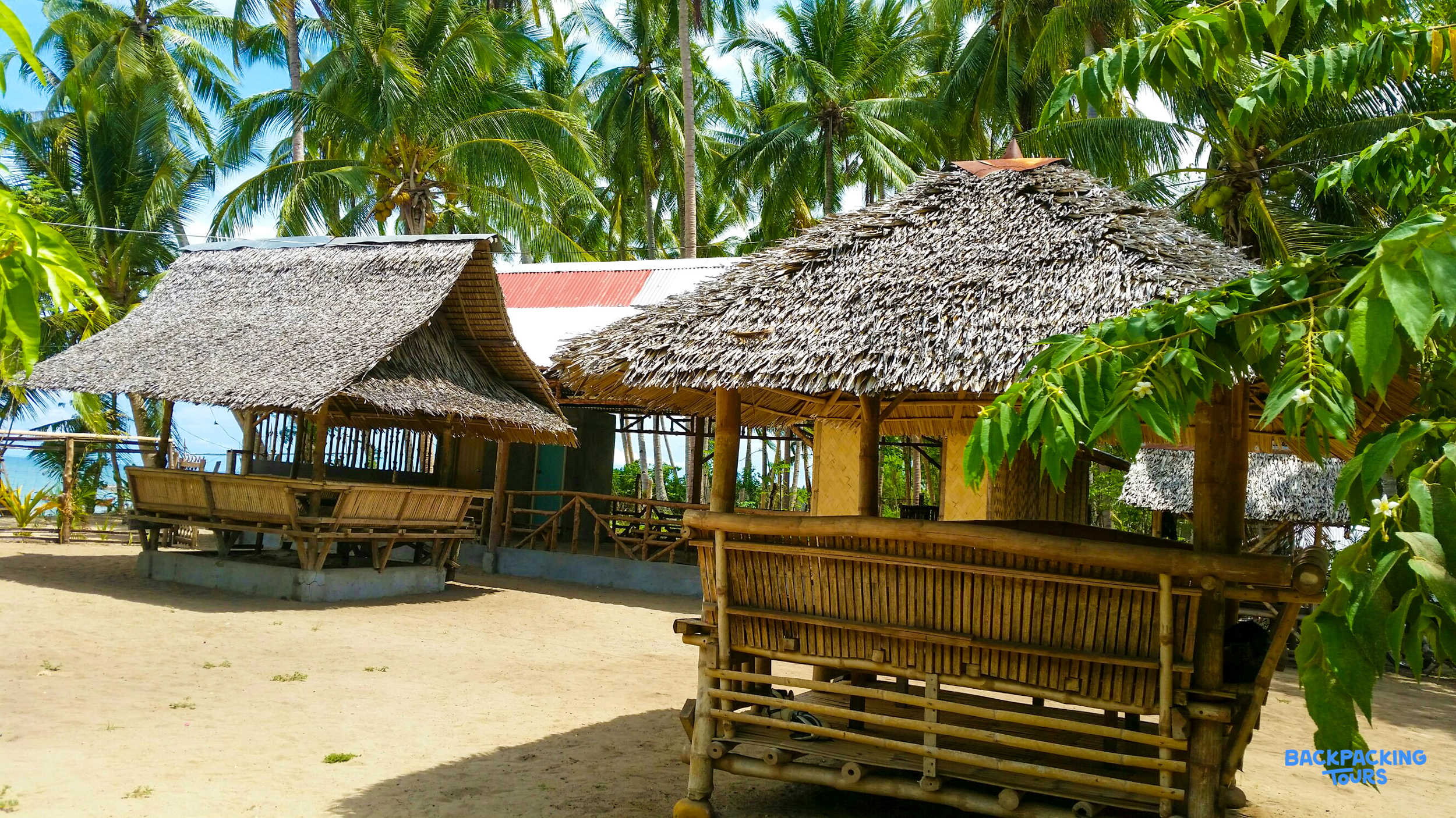 Relaxing bamboo huts with thatched roofs on a sandy beach, surrounded by palm trees in the Philippines.