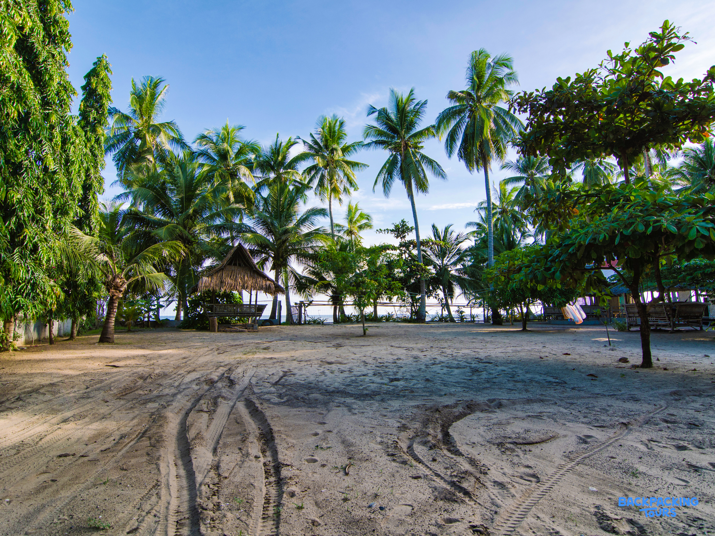 Relaxing sandy beach accommodation with a small hut and lush palm trees under a blue sky.