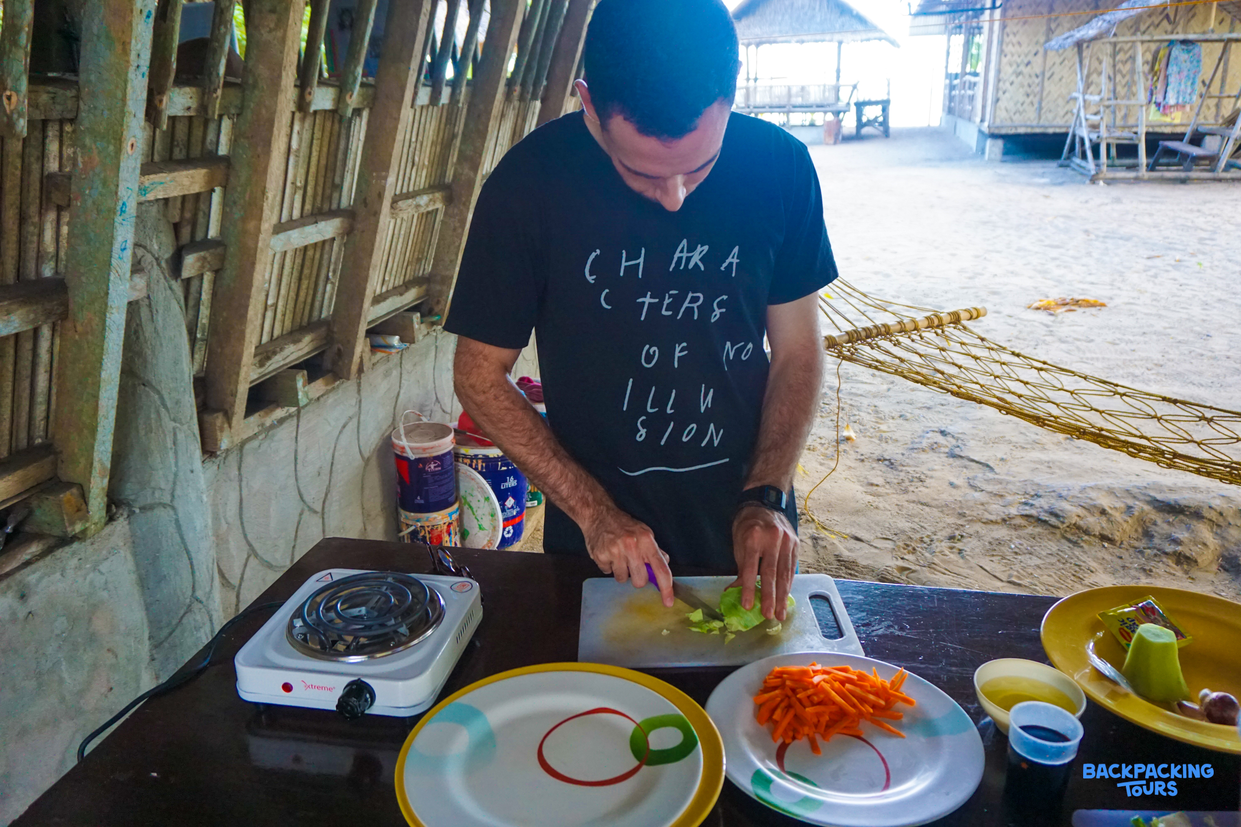 A man chops fresh vegetables for a meal in a rustic, open-air kitchen by the beach.