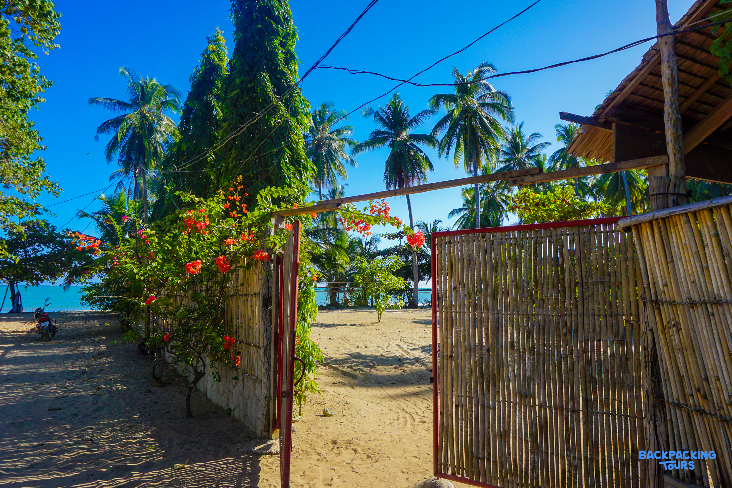 An inviting bamboo gate opens to a sandy path leading to a tropical beach.