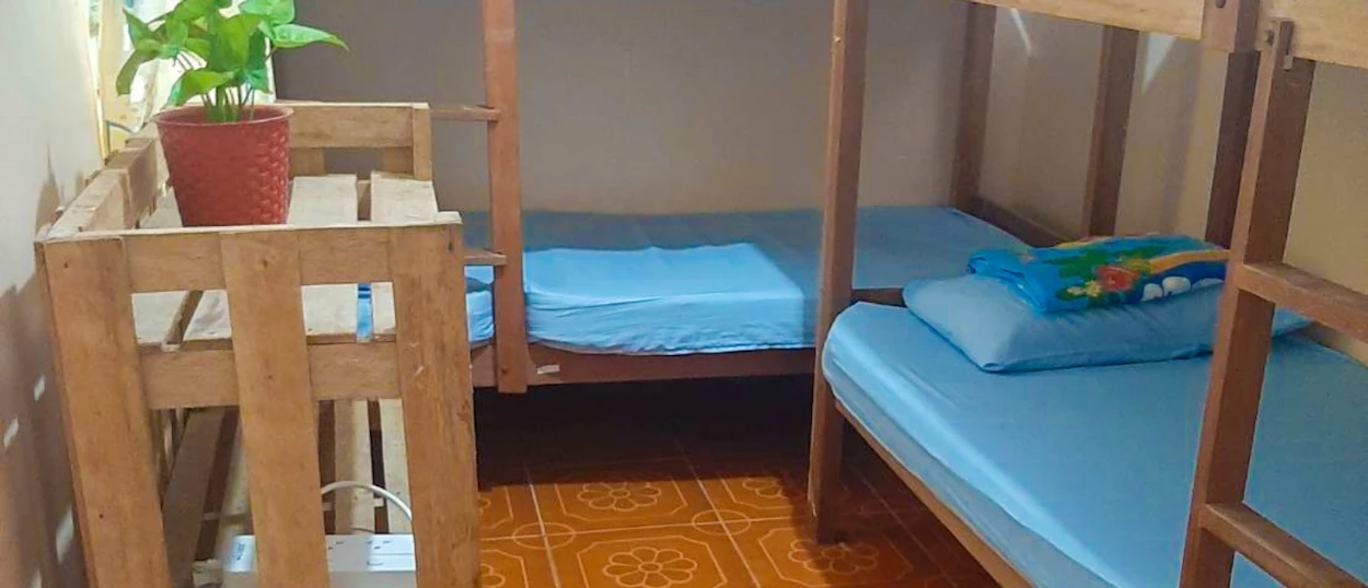 A welcoming hostel dorm room with multiple wooden bunk beds, blue sheets, and patterned floor tiles.