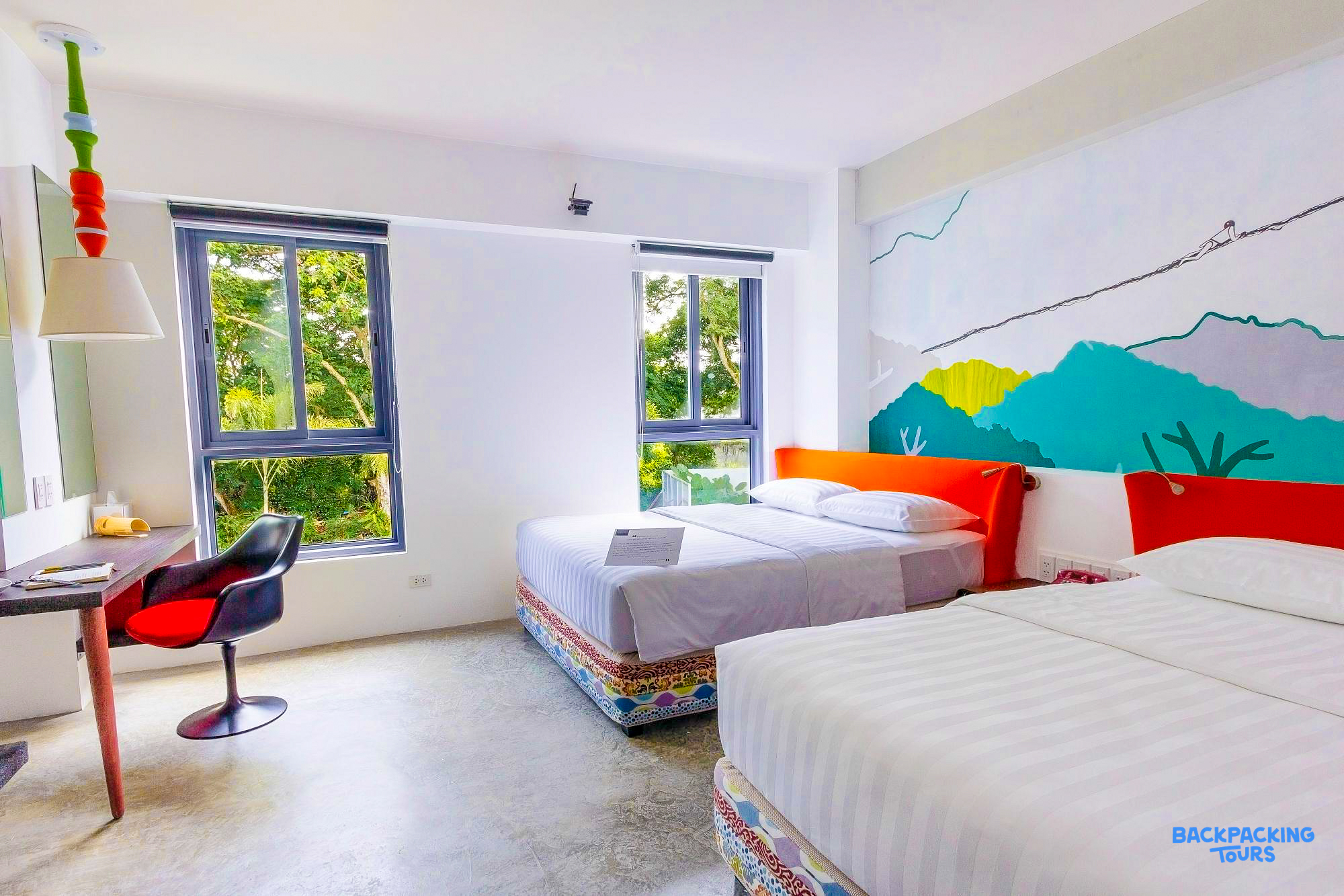 A bright and modern hotel room in Puerto Princesa with two comfortable beds and a colorful wall mural.