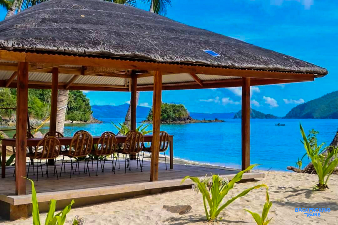 Relaxing open-air dining hut on a sandy beach with clear blue waters in Port Barton, Philippines.