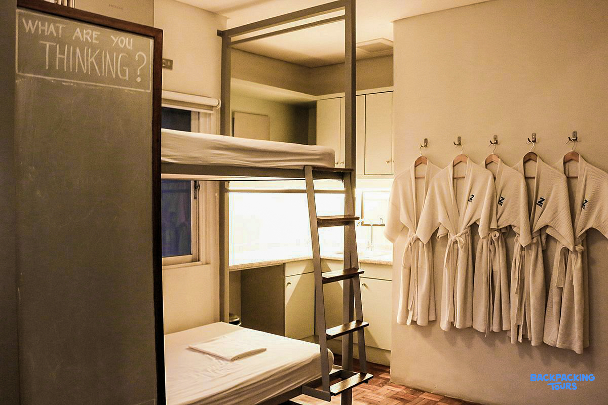 A clean, modern hostel room in Manila with bunk beds, a kitchenette, and bathrobes.