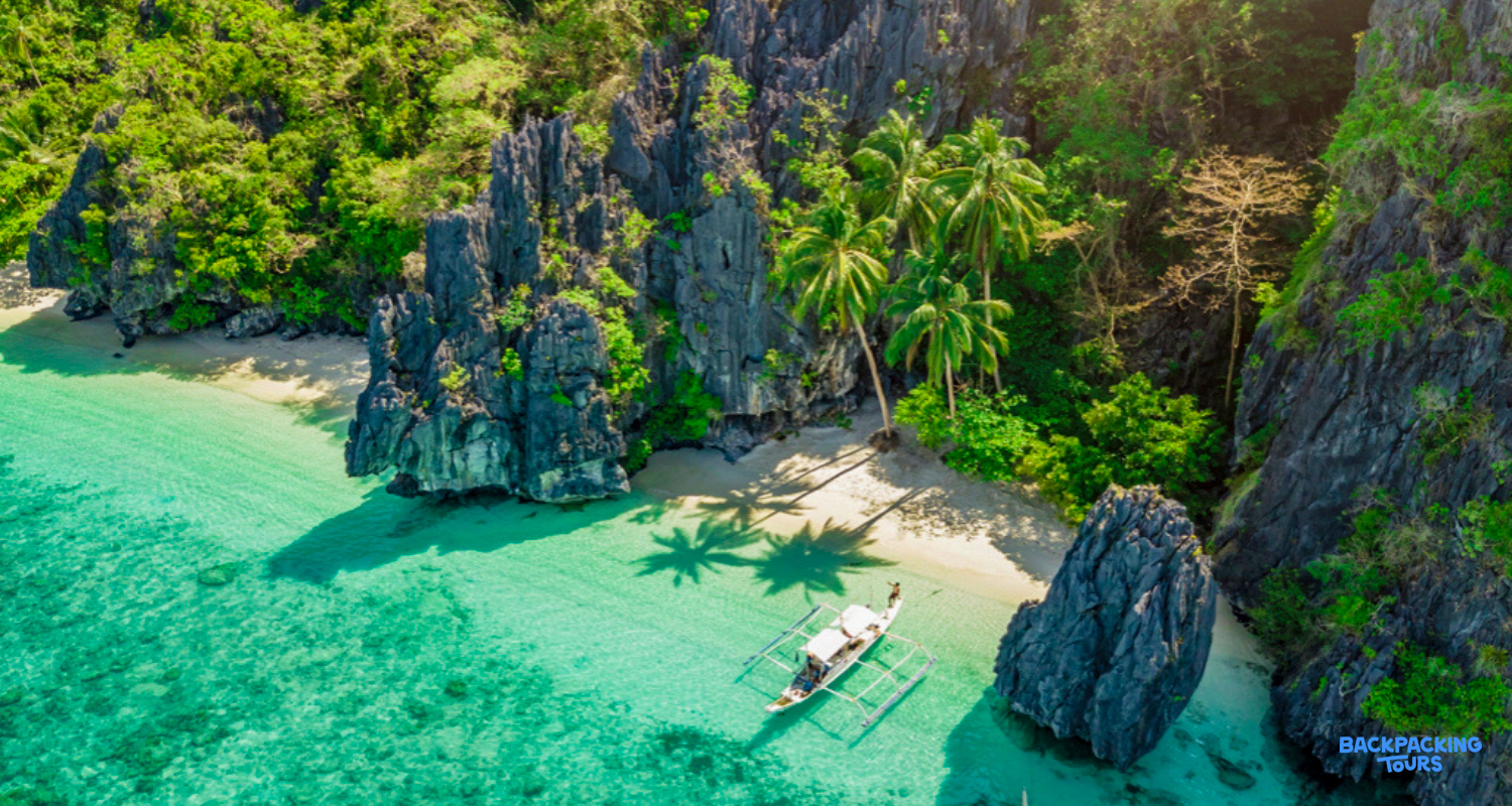 Aerial view of a traditional boat on a pristine beach with turquoise water and limestone cliffs, Coron.